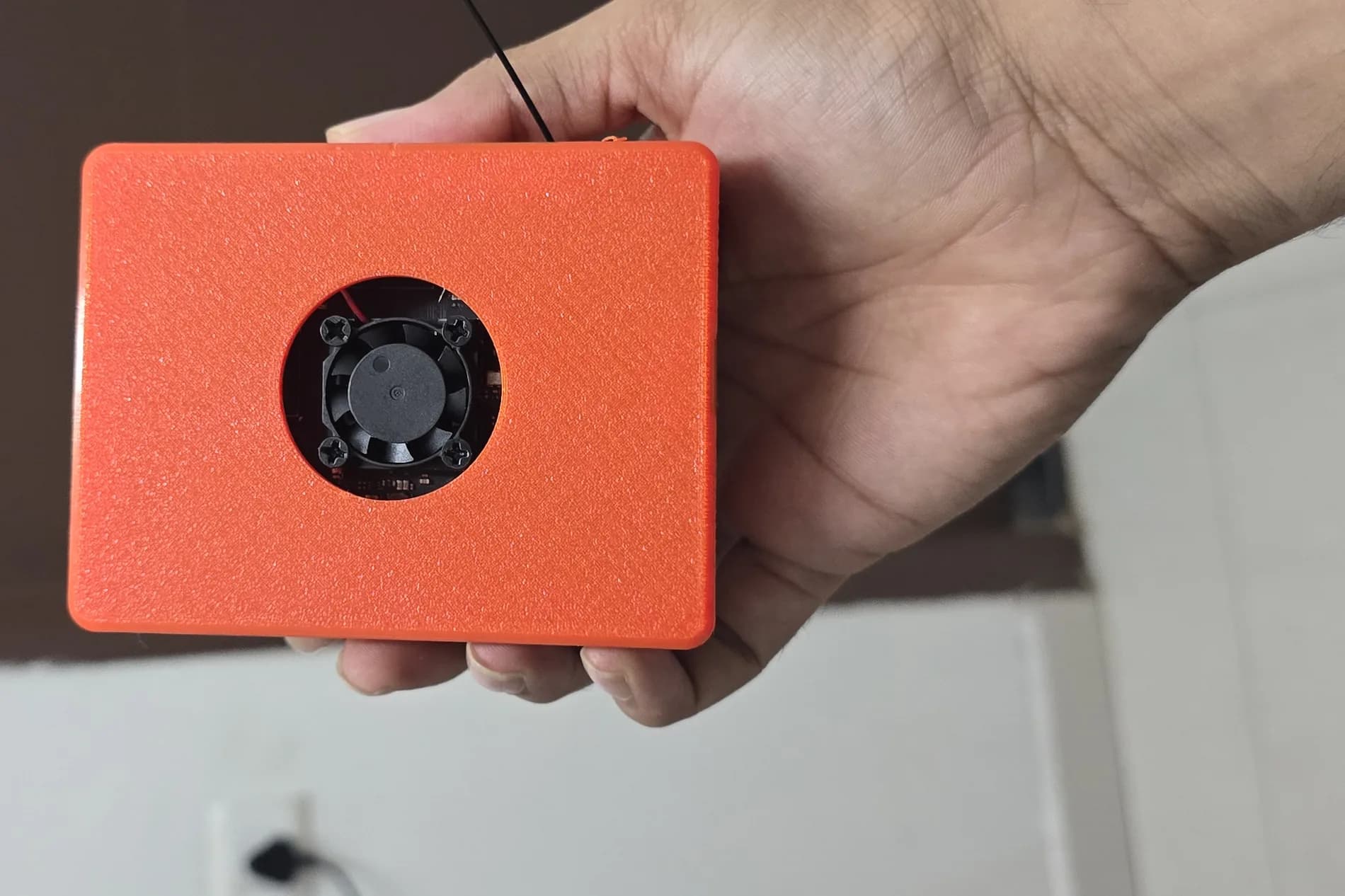 The SK-01 prototype held in one hand, showing its cooling fan and 3D-printed orange enclosure.
